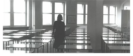 Foto: Eine Frau steht verloren in einem Raum mit quadratischen Tischen