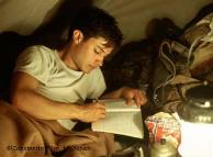 Ein junger Mann liegt in einem Zelt und schreibt in ein Heft