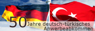 Banner zum 50-jährigen Jubiläum des deutsch-türkischen Anwerbeabkommens mit Deutschlandfahne und Türkeifahne im Hintergrund