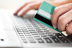 Mit einer Kreditkarte in der Hand bestellt ein Verbraucher mit seinem Laptop Waren im Internet