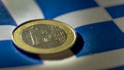Euromünze liegt auf griechischer Fahne